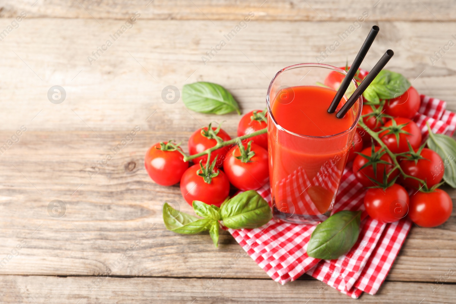 Photo of Tasty tomato juice in glass with basil leaves and fresh vegetables on wooden table, space for text