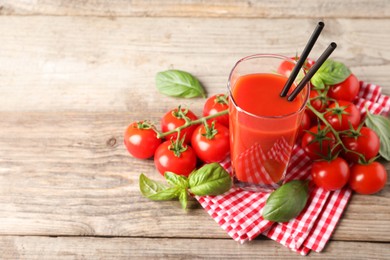 Tasty tomato juice in glass with basil leaves and fresh vegetables on wooden table, space for text