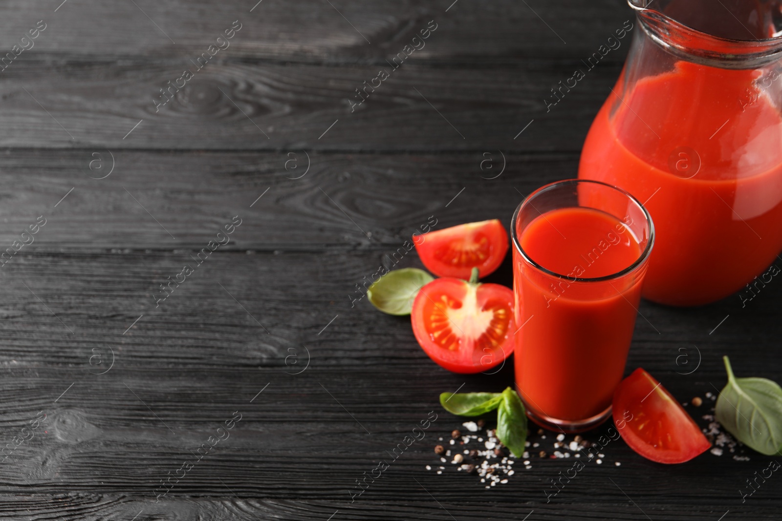 Photo of Tasty tomato juice with fresh vegetables and spices on black wooden table, space for text