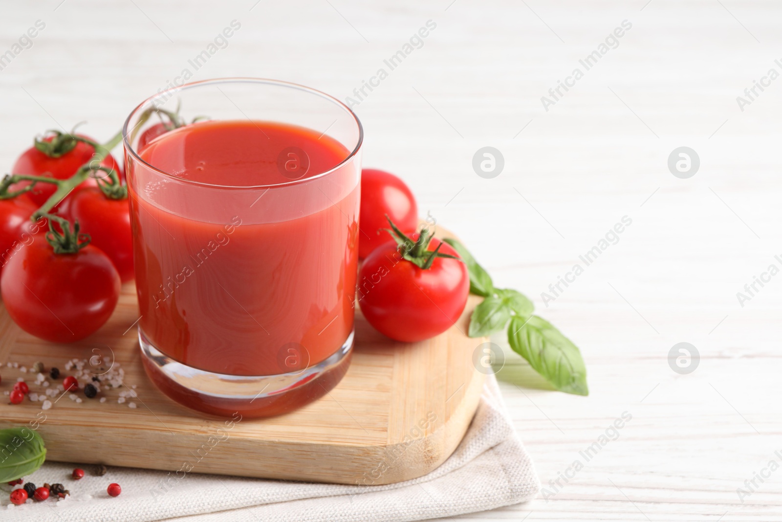 Photo of Tasty tomato juice in glass with fresh vegetables and spices on white wooden table, space for text