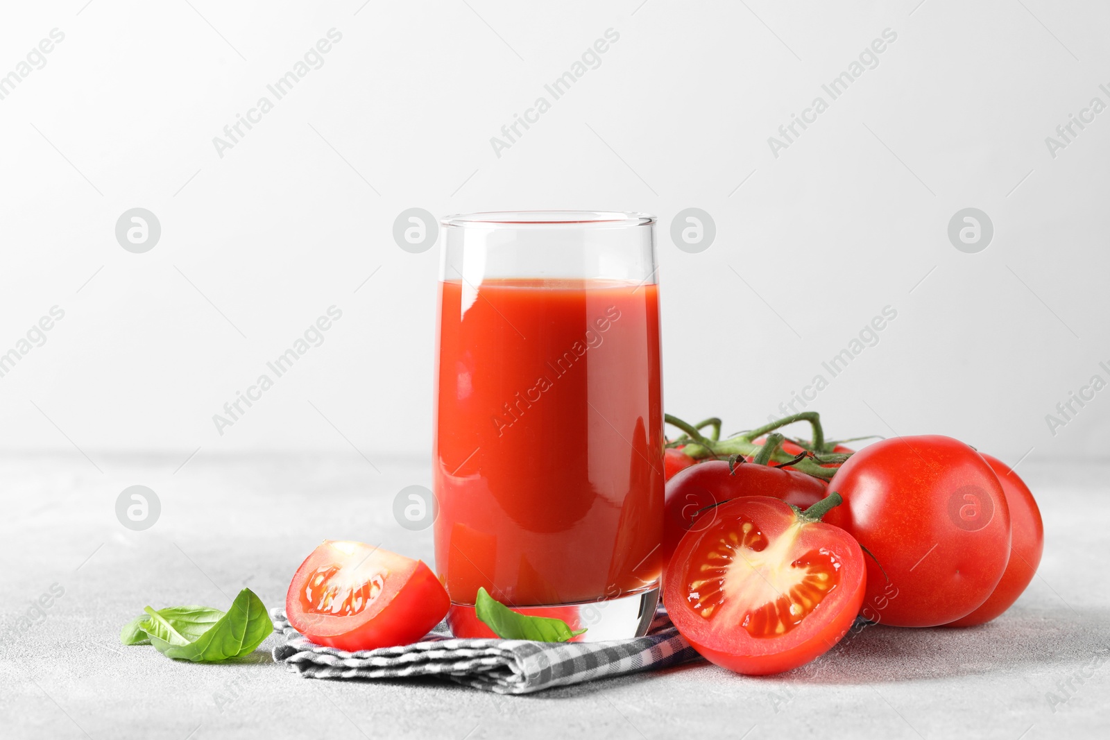 Photo of Tasty tomato juice in glass with fresh vegetables and basil leaves on light grey table