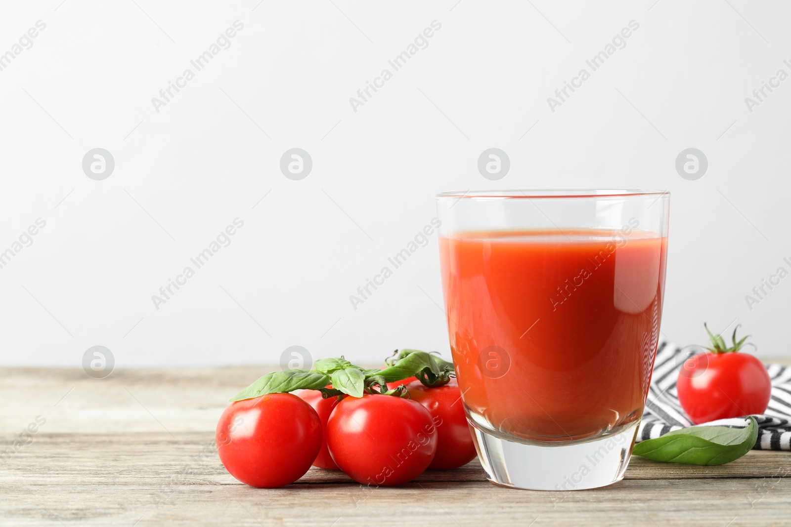 Photo of Tasty tomato juice in glass, basil leaves and fresh vegetables on wooden table, space for text