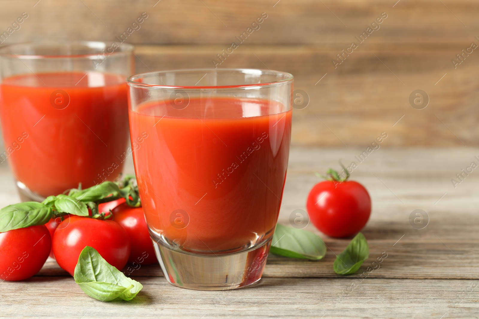 Photo of Tasty tomato juice in glasses, basil leaves and fresh vegetables on wooden table, closeup