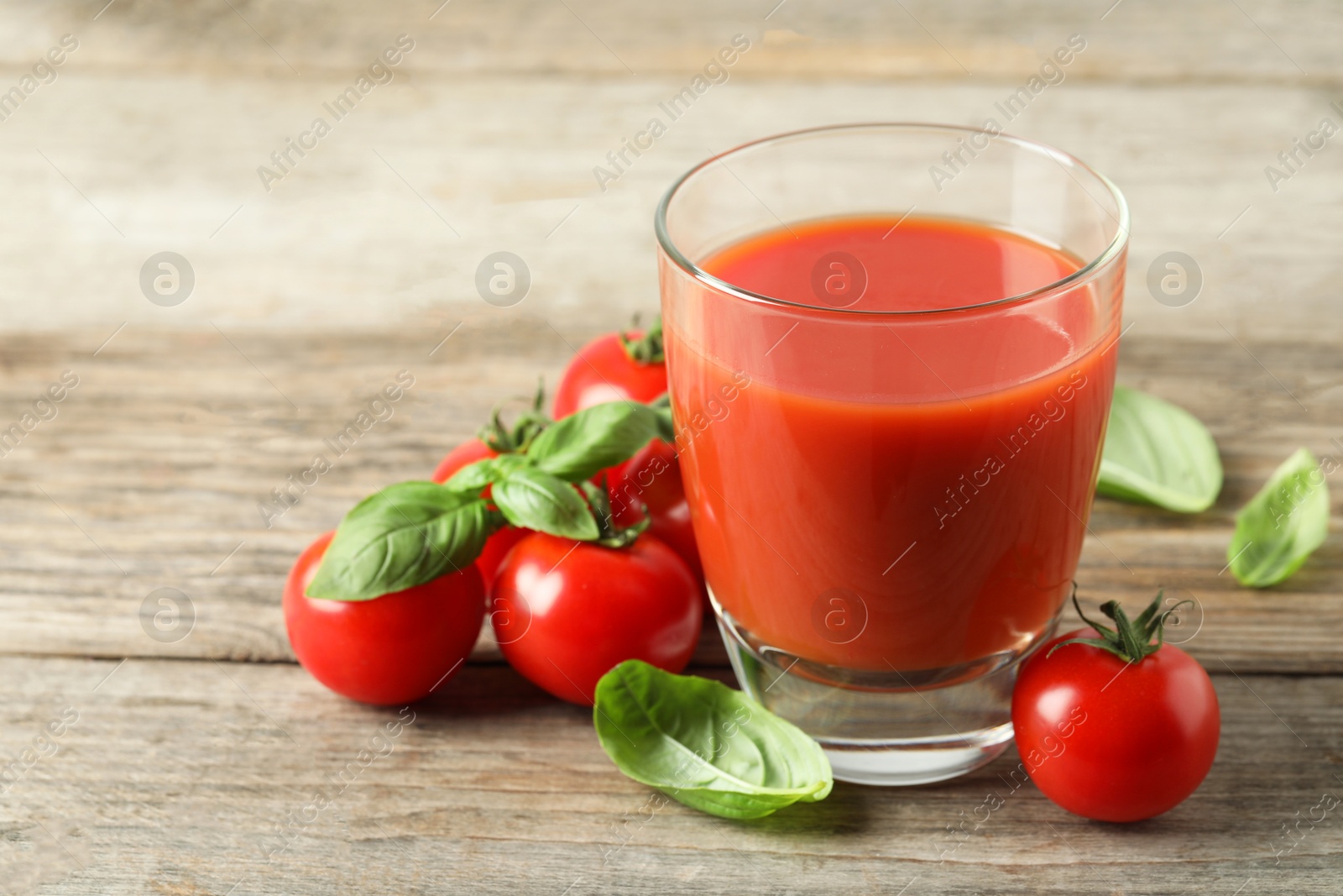 Photo of Tasty tomato juice in glass, basil leaves and fresh vegetables on wooden table, closeup