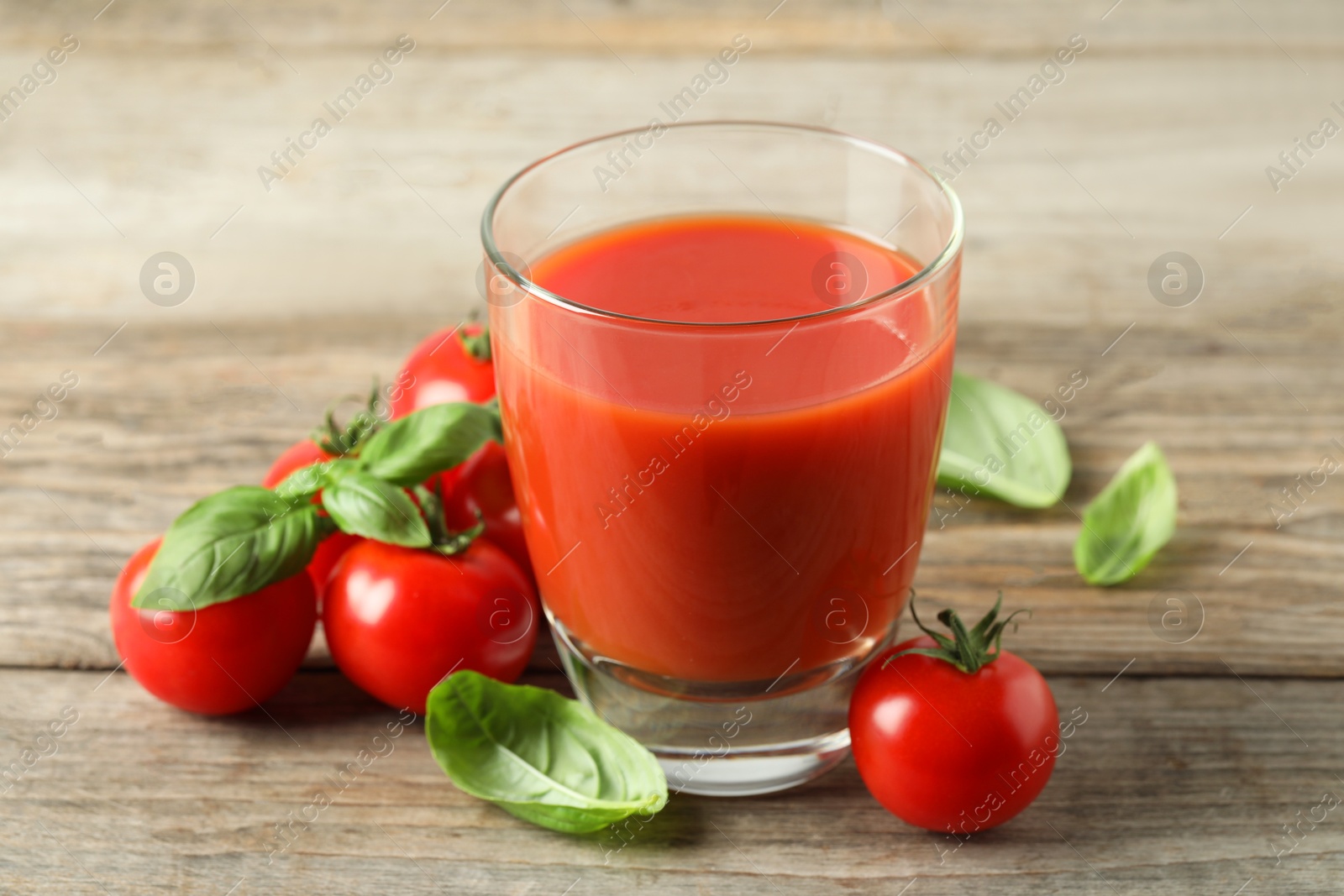 Photo of Tasty tomato juice in glass, basil leaves and fresh vegetables on wooden table, closeup