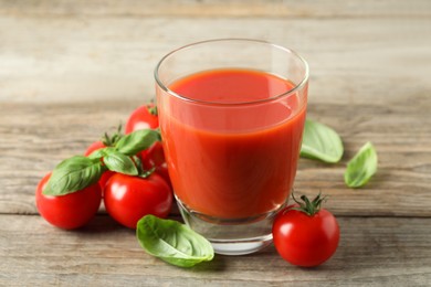 Tasty tomato juice in glass, basil leaves and fresh vegetables on wooden table, closeup