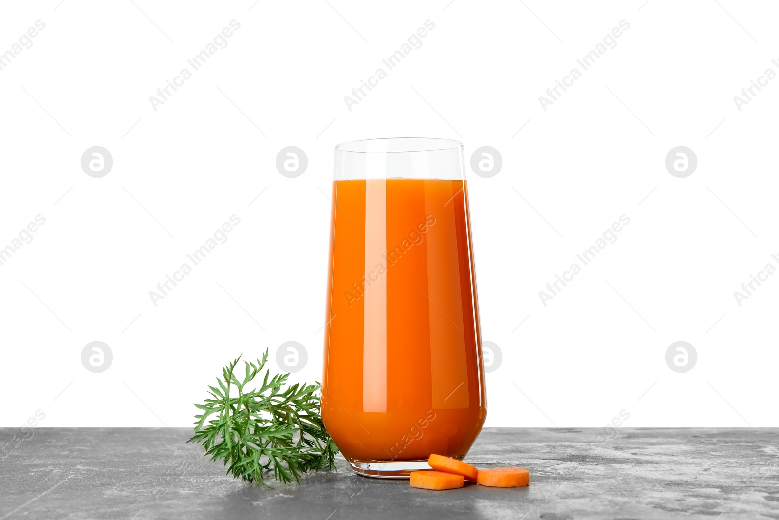 Photo of Fresh carrot juice in glass and cut vegetable on grey textured table against white background