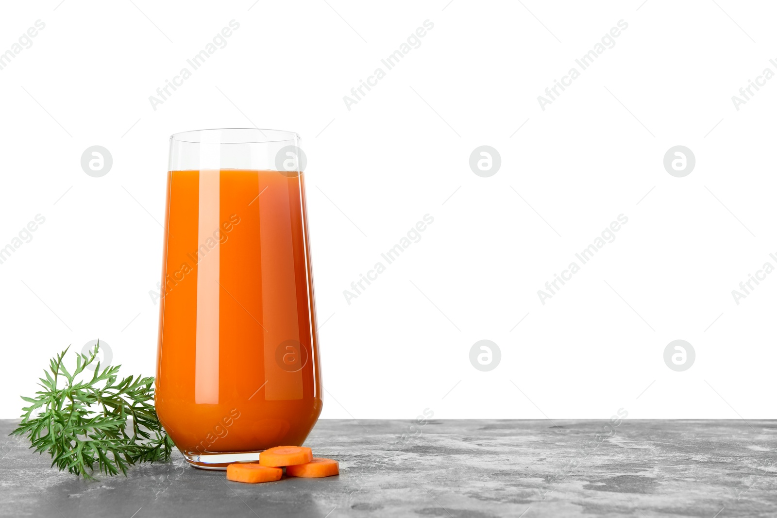 Photo of Fresh carrot juice in glass and cut vegetable on grey textured table against white background. Space for text