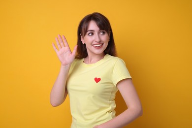 Happy young woman waving on orange background