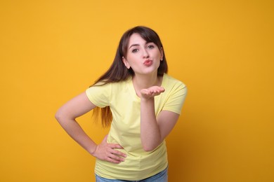 Beautiful woman blowing kiss on orange background