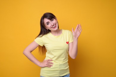 Photo of Happy young woman waving on orange background