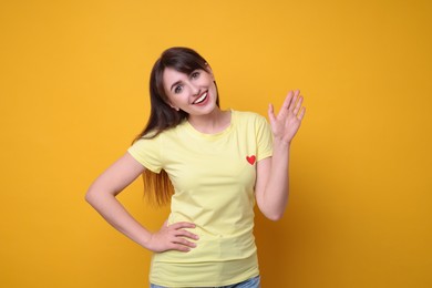 Happy young woman waving on orange background