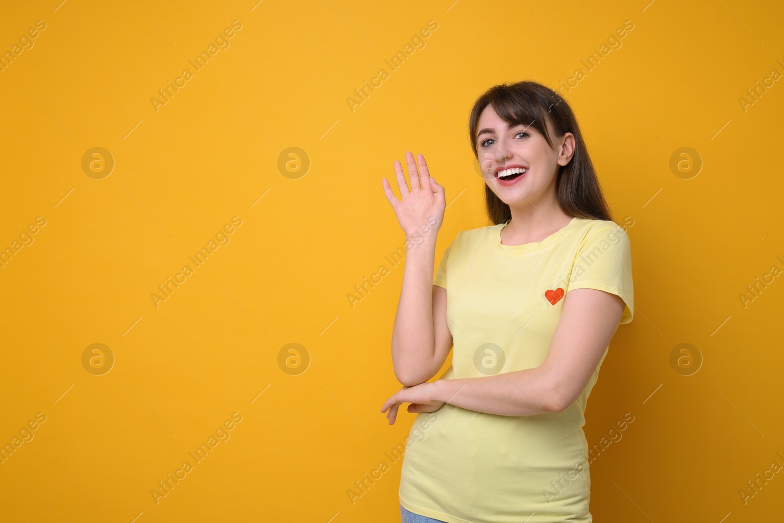 Photo of Happy young woman waving on orange background, space for text