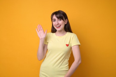 Photo of Happy young woman waving on orange background