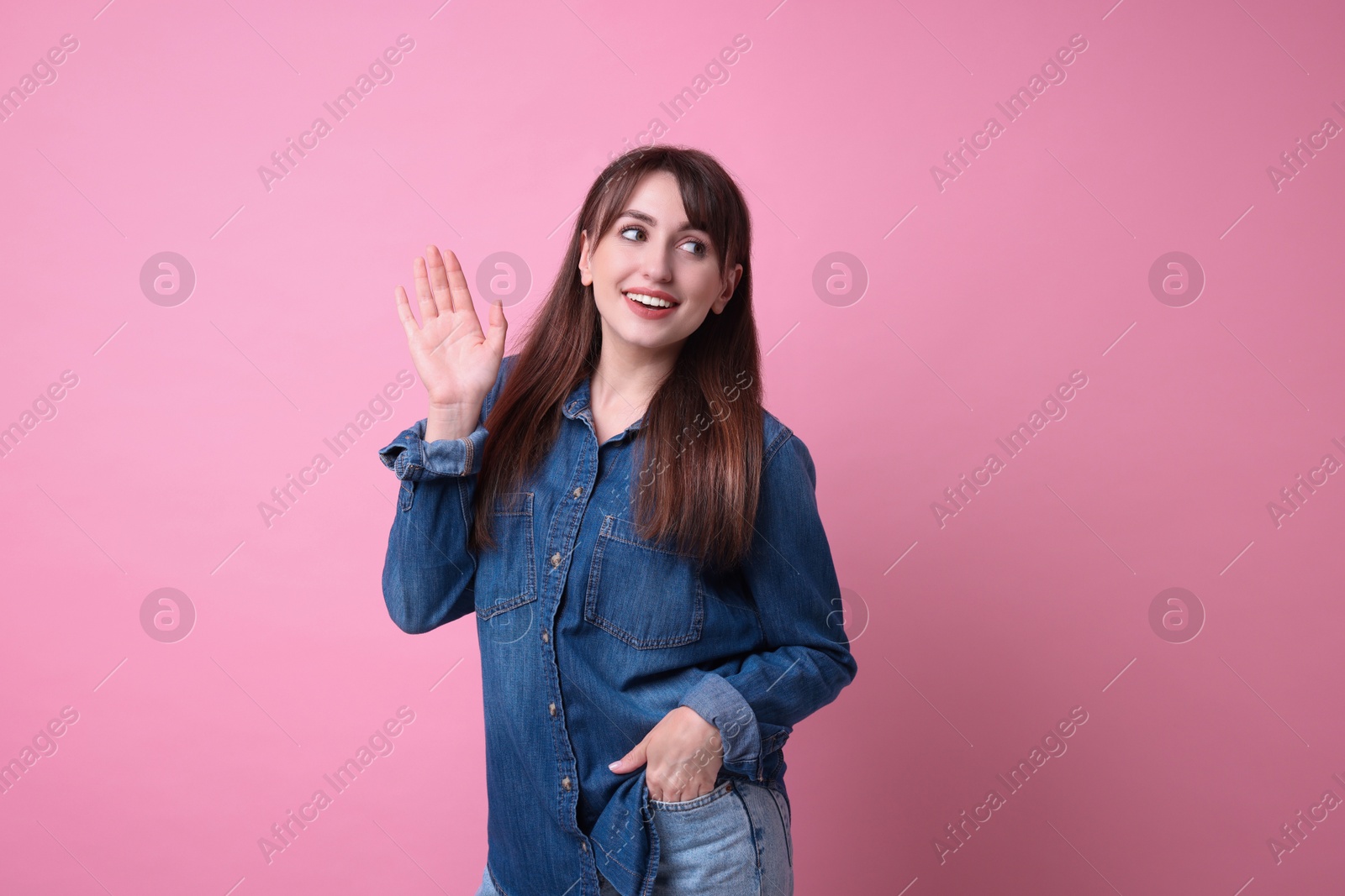 Photo of Happy young woman waving on pink background