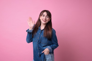 Happy young woman waving on pink background