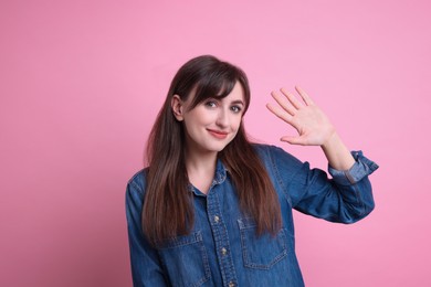 Happy young woman waving on pink background