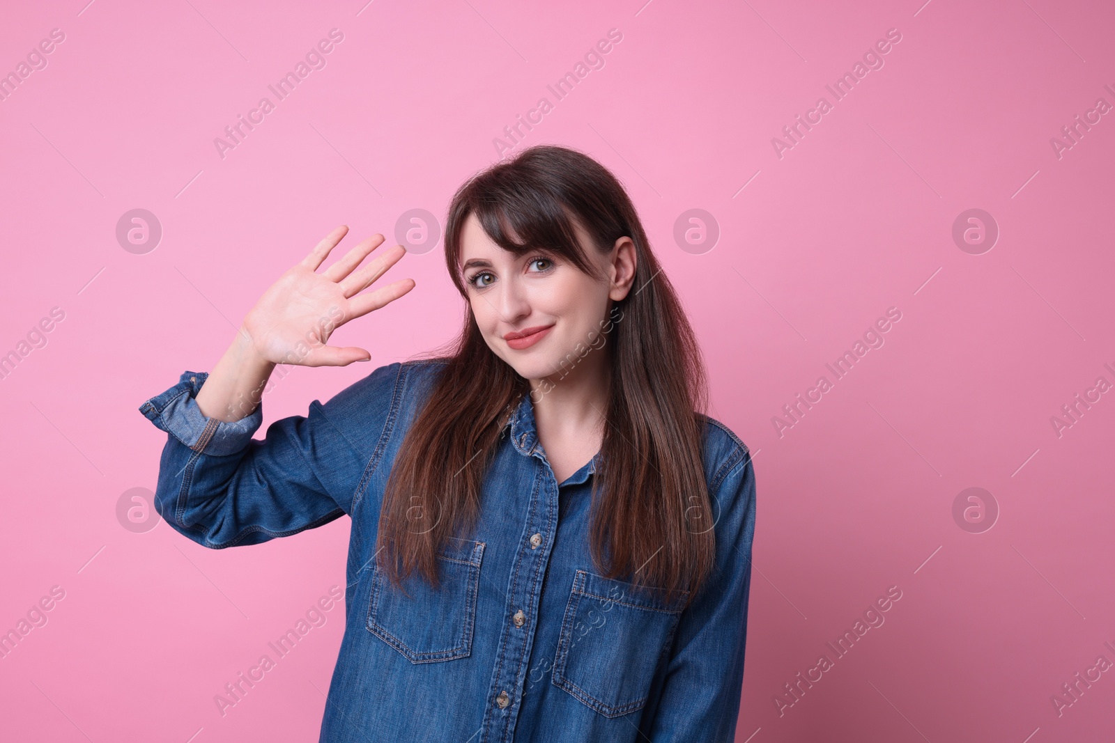 Photo of Happy young woman waving on pink background