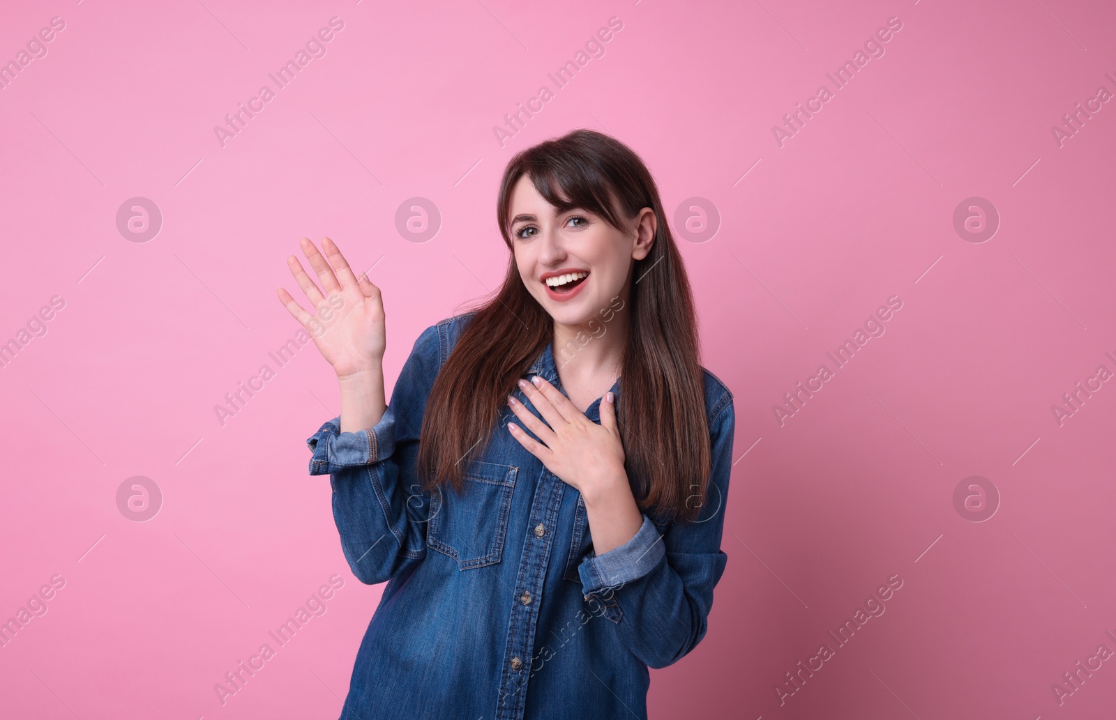 Photo of Happy young woman waving on pink background