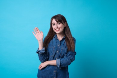Photo of Happy woman waving on light blue background