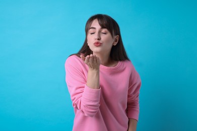 Beautiful woman blowing kiss on light blue background