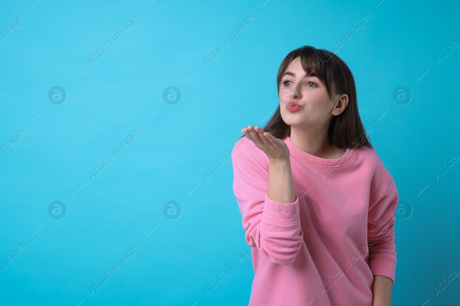 Photo of Beautiful woman blowing kiss on light blue background, space for text