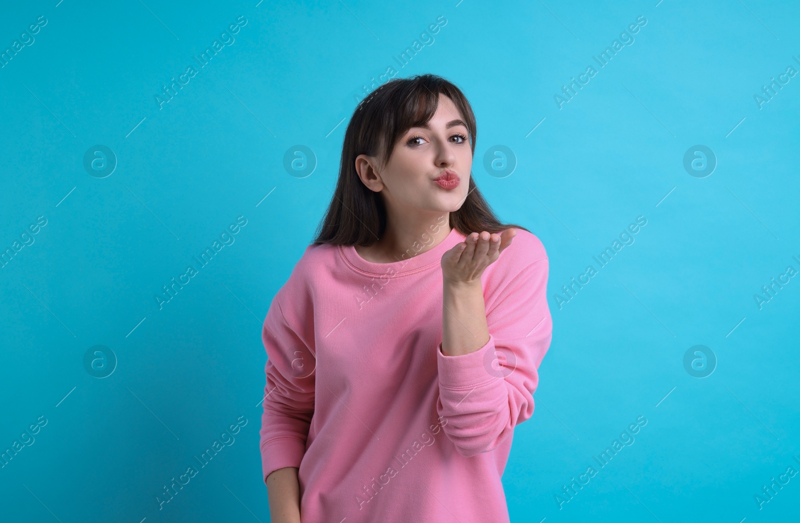 Photo of Beautiful woman blowing kiss on light blue background