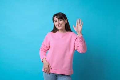 Photo of Happy woman waving on light blue background