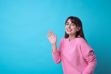 Happy woman waving on light blue background, space for text