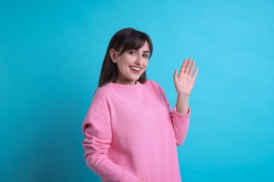 Photo of Happy woman waving on light blue background