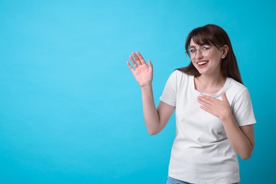 Happy woman waving on light blue background, space for text