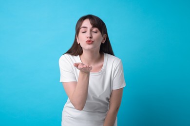 Photo of Beautiful woman blowing kiss on light blue background