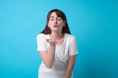 Beautiful woman blowing kiss on light blue background