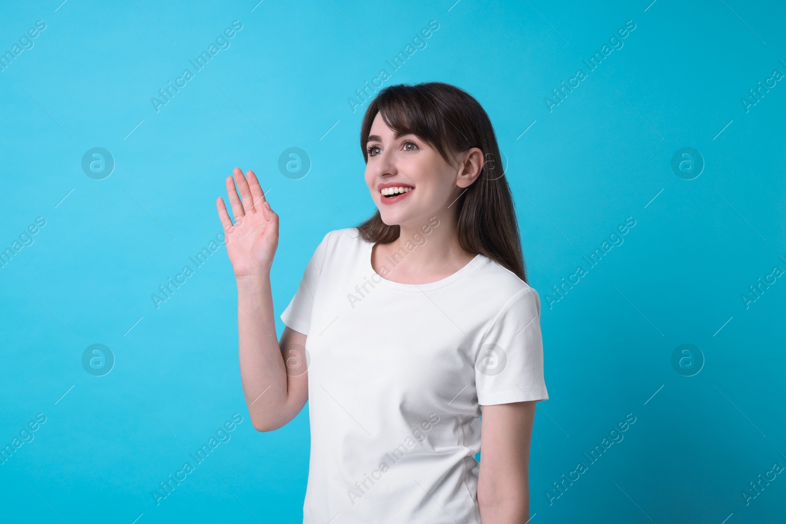 Photo of Happy woman waving on light blue background