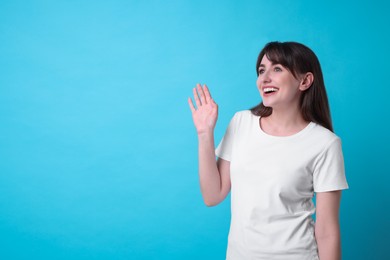 Happy woman waving on light blue background, space for text