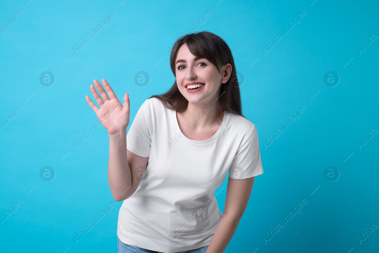 Photo of Happy woman waving on light blue background