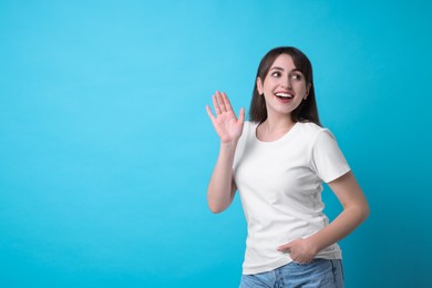 Photo of Happy woman waving on light blue background, space for text