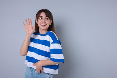 Happy woman waving on light grey background, space for text