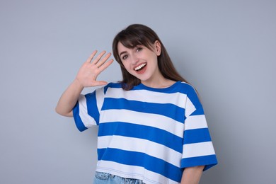 Happy woman waving on light grey background