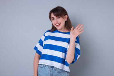 Happy woman waving on light grey background