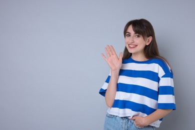 Happy woman waving on light grey background, space for text