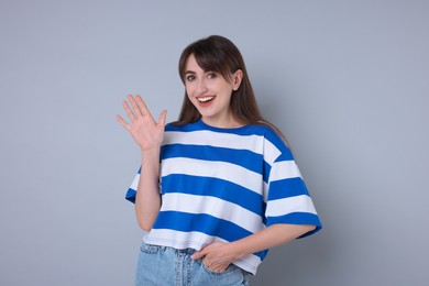 Happy woman waving on light grey background