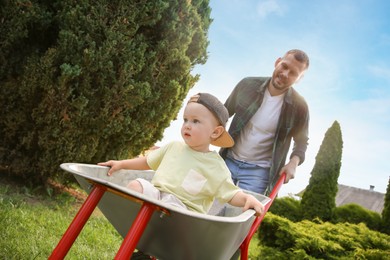 Photo of Father pushing wheelbarrow with his son outdoors, selective focus