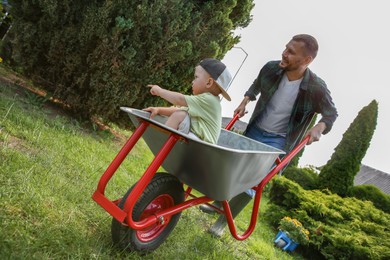 Photo of Father pushing wheelbarrow with his son outdoors