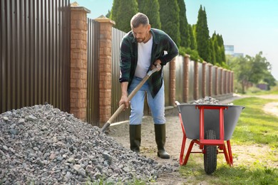 Photo of Man picking stones up with shovel and wheelbarrow outdoors