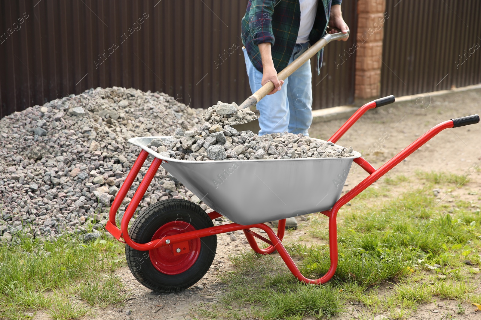 Photo of Man with shovel loading stones into wheelbarrow outdoors, closeup