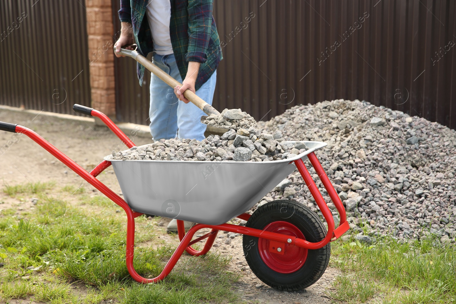 Photo of Man with shovel loading stones into wheelbarrow outdoors, closeup