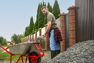 Photo of Man with shovel loading stones into wheelbarrow outdoors