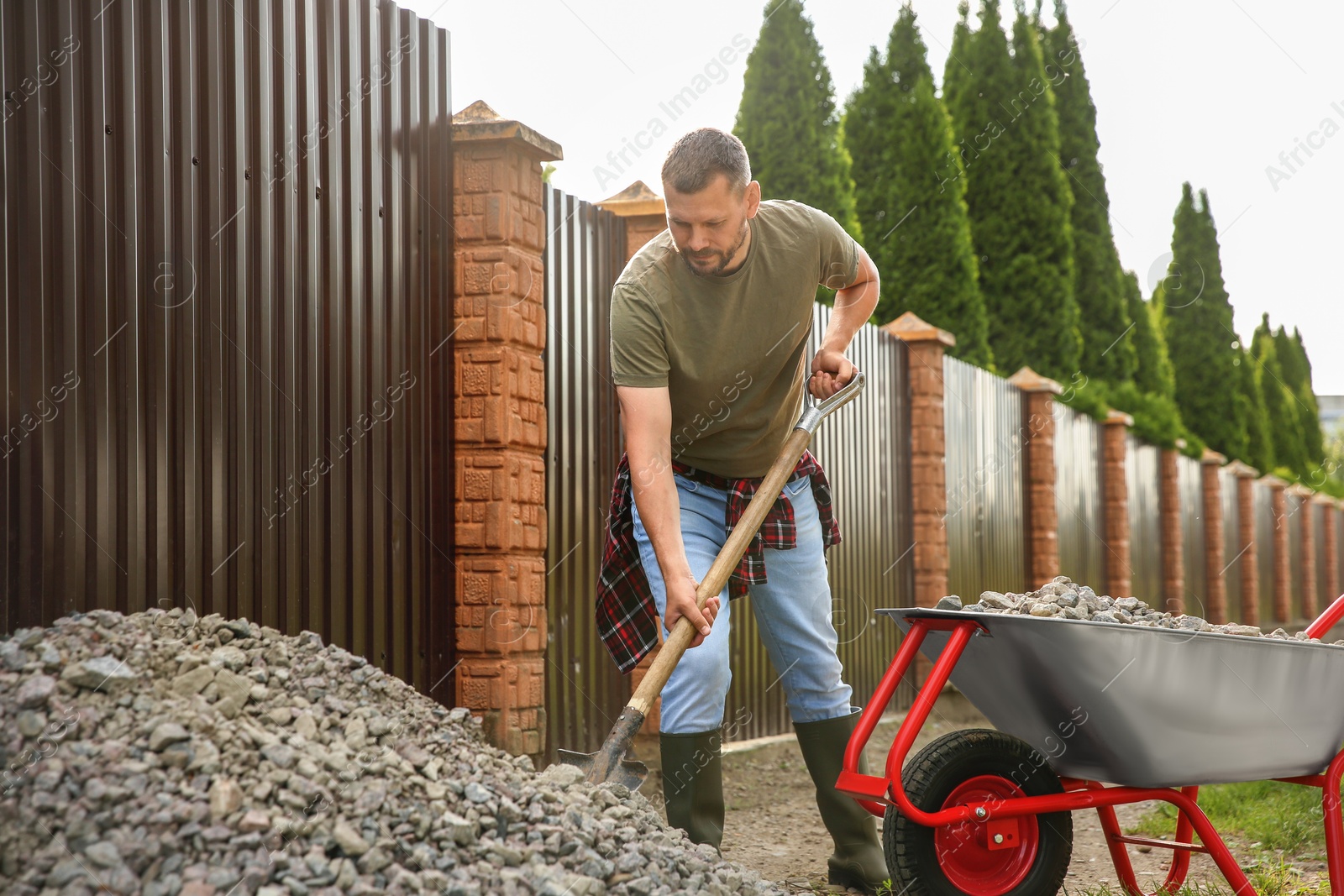 Photo of Man picking stones up with shovel and wheelbarrow outdoors