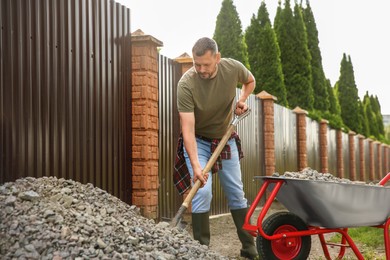 Man picking stones up with shovel and wheelbarrow outdoors